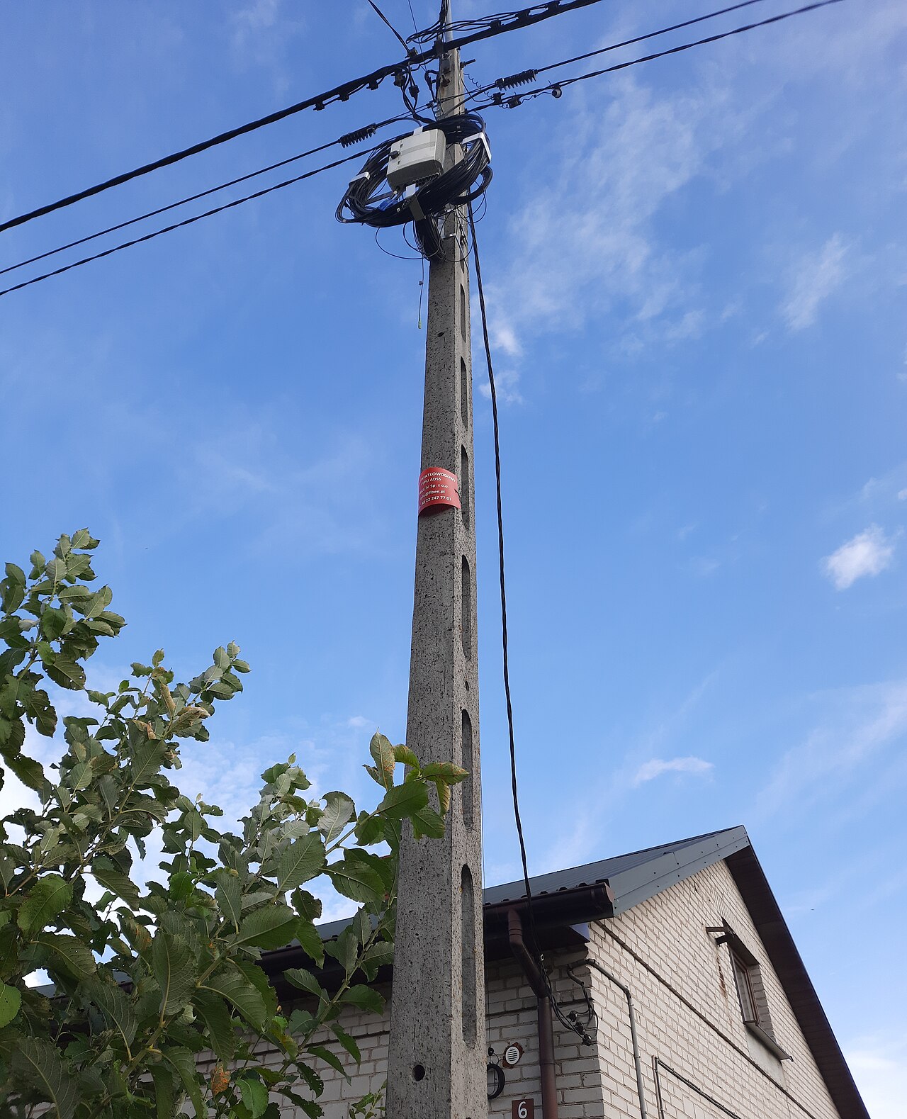 Aerial all-dielectric self-supporting (ADSS) fiber optic cable strung to a utility pole, with a service loop and FTTH patch enclosure against a blue sky